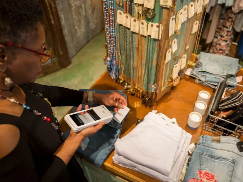 An associate scans a barcode with a Clover Flex among folded jeans at a boutique