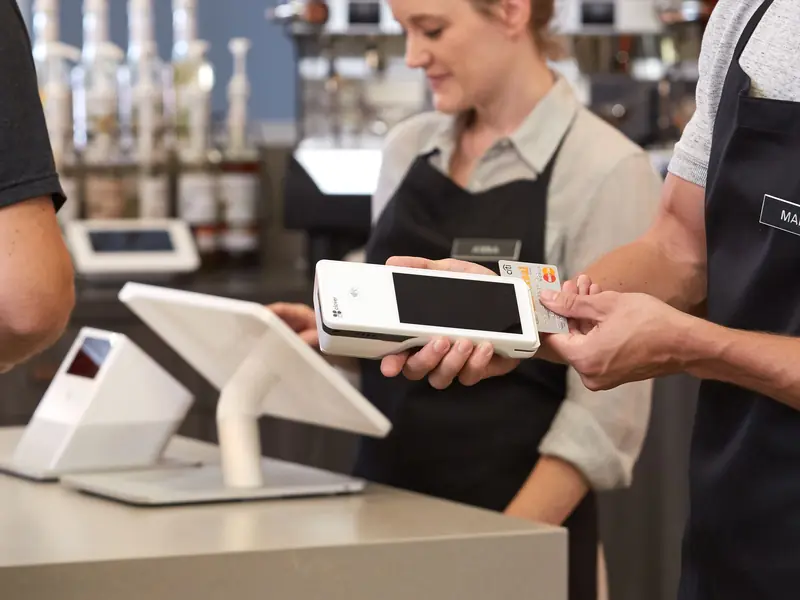 A barista hands a Clover Flex across a cafe counter so a customer can pay