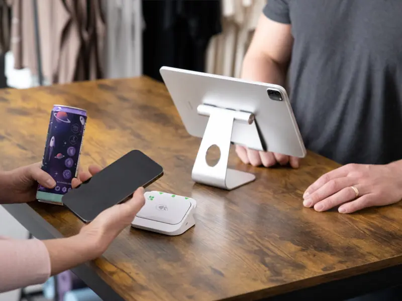 A customer taps a phone on a Clover Go reader at a wooden shop counter