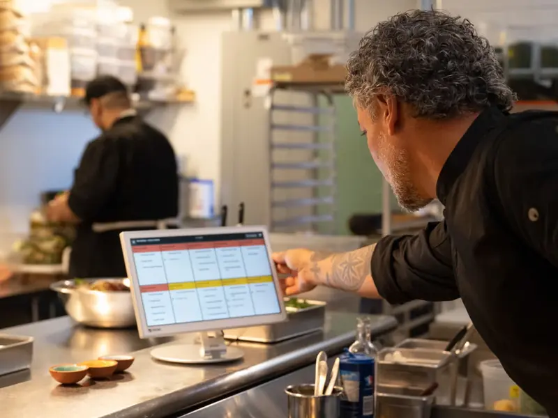 A chef reads open orders on a Clover Kitchen Display in a restaurant kitchen