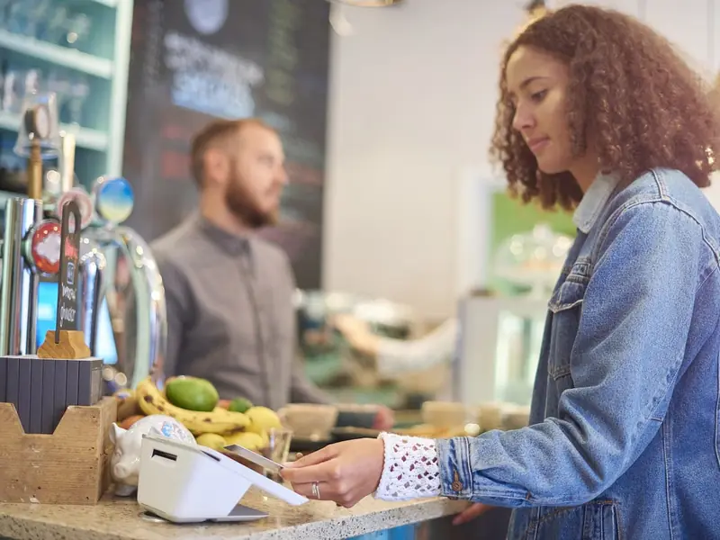 A customer taps to pay on a Clover Mini at a cafe and market counter