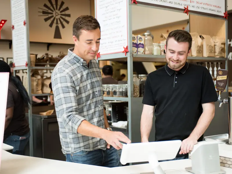 Two cafe employees work together at a Clover Station behind the counter