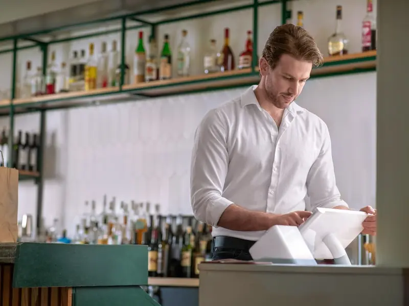 A bartender enters an order on a Clover Station Solo behind a stocked bar